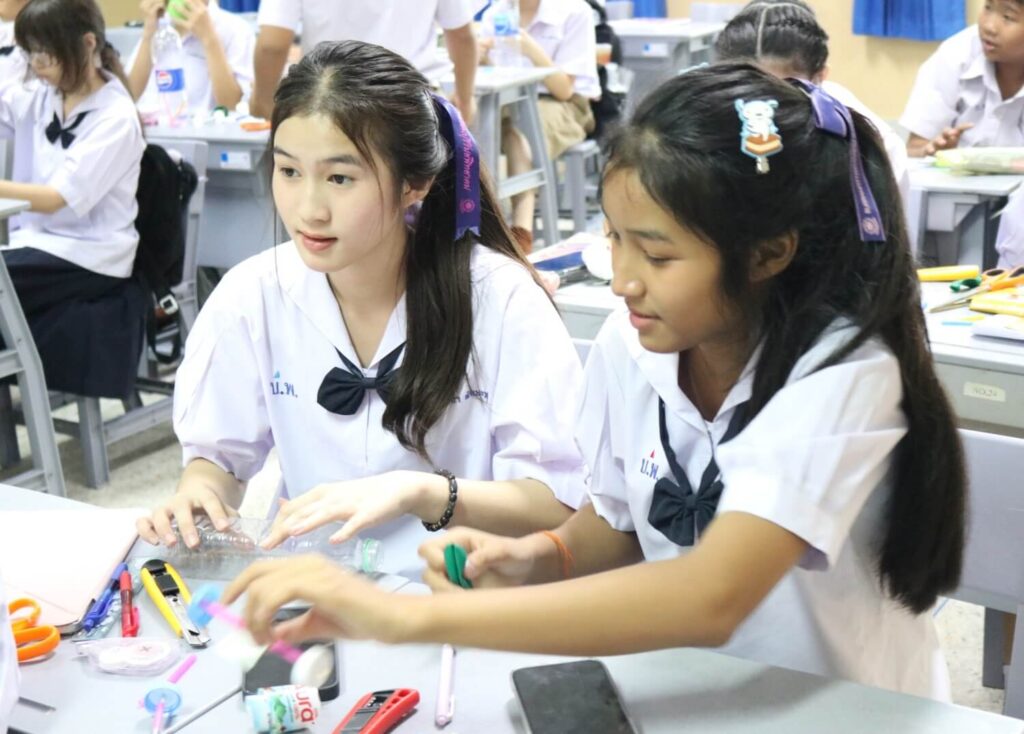 Buriram Pitthayakhom (BP) School students in white uniforms working on a craft project at their desk in a classroom
