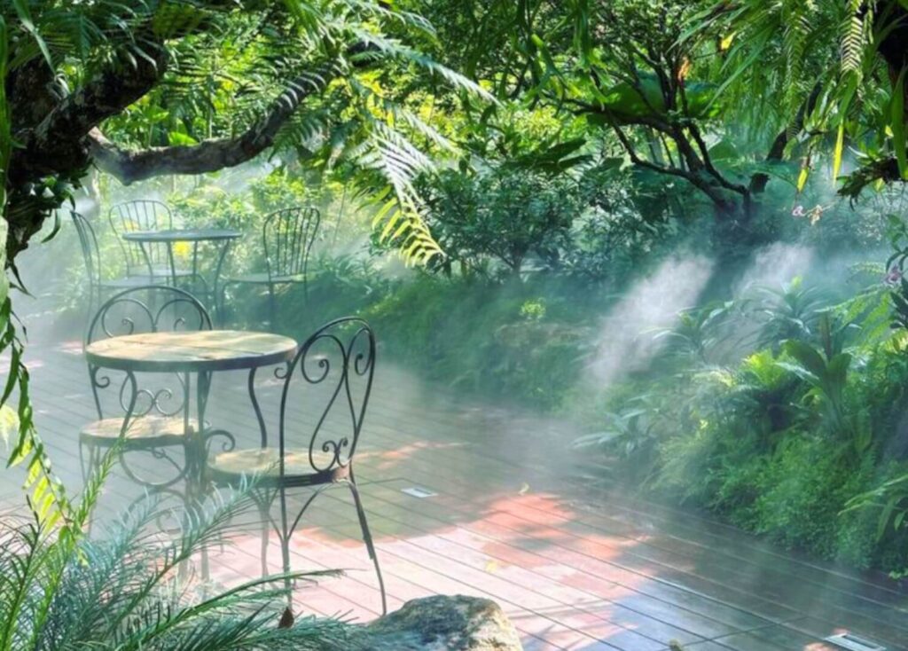 Misty garden café with empty wrought-iron tables surrounded by lush greenery.