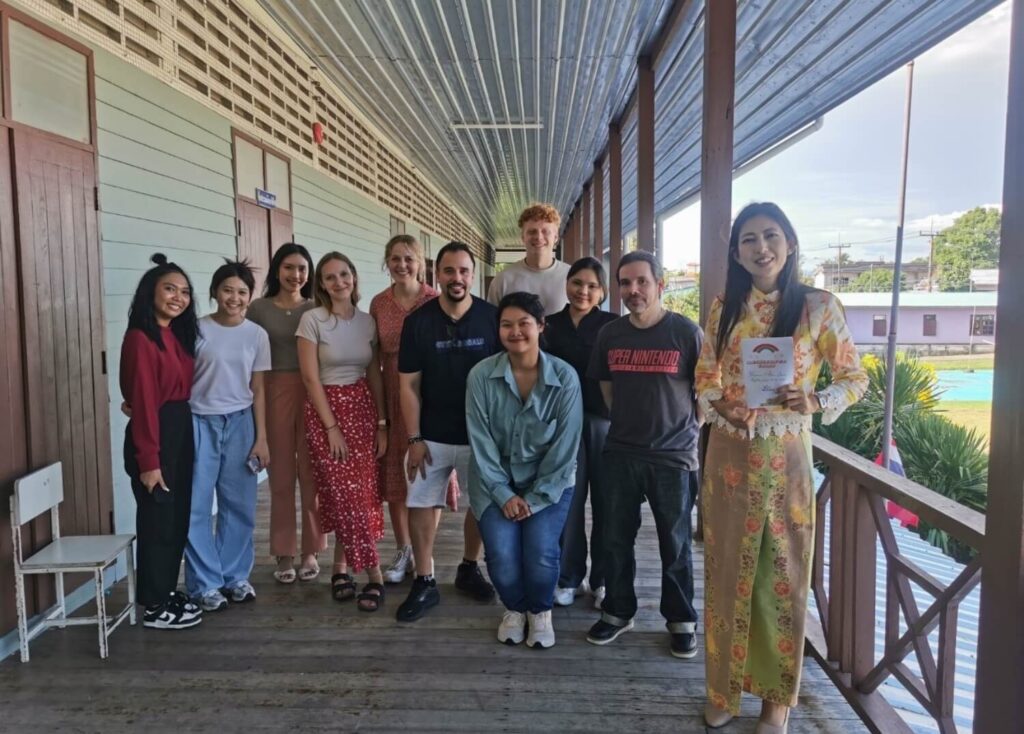 Teacher Millie Rose Hogman with fellow BFITS educators and Baan Ar Jor team posing in the Baan Mhai Khao School hallway for a group photo